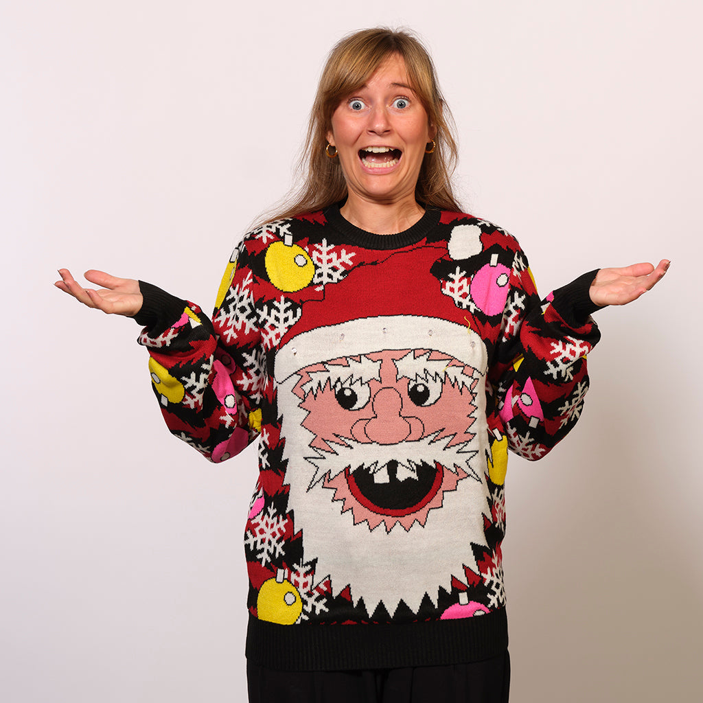 En dame poserer med hænderne i vejret iført en julesweater.